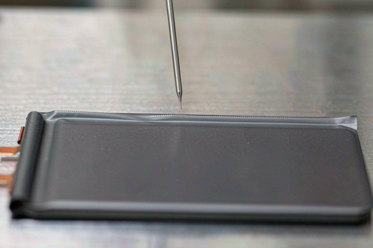 Semi-solid state battery helium leak screening: a sniffer probe tip above a pouch cell heat seal on a stainless steel fixture