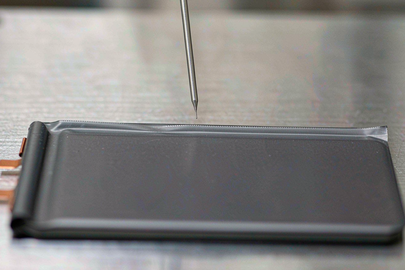 Semi-solid state battery helium leak screening: a sniffer probe tip above a pouch cell heat seal on a stainless steel fixture